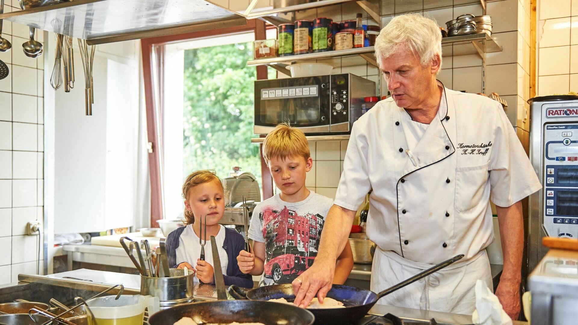 Koch erklärt Kindern in der Küche die Zubereitung eines Gerichtes