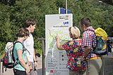 Wanderer orientieren sich an einer Informationstafel auf dem Bahnsteig