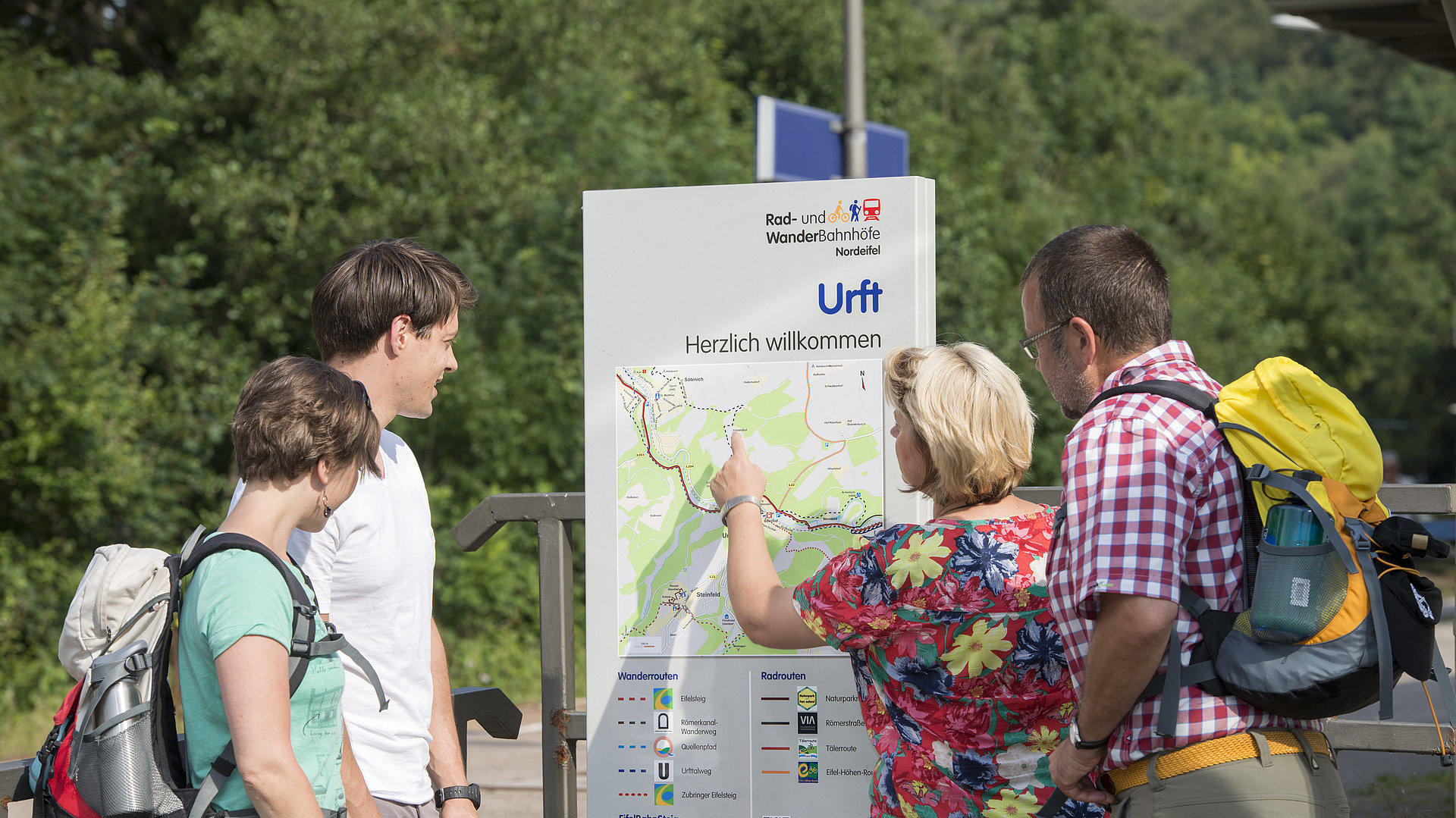 Wanderer orientieren sich an einer Informationstafel auf dem Bahnsteig