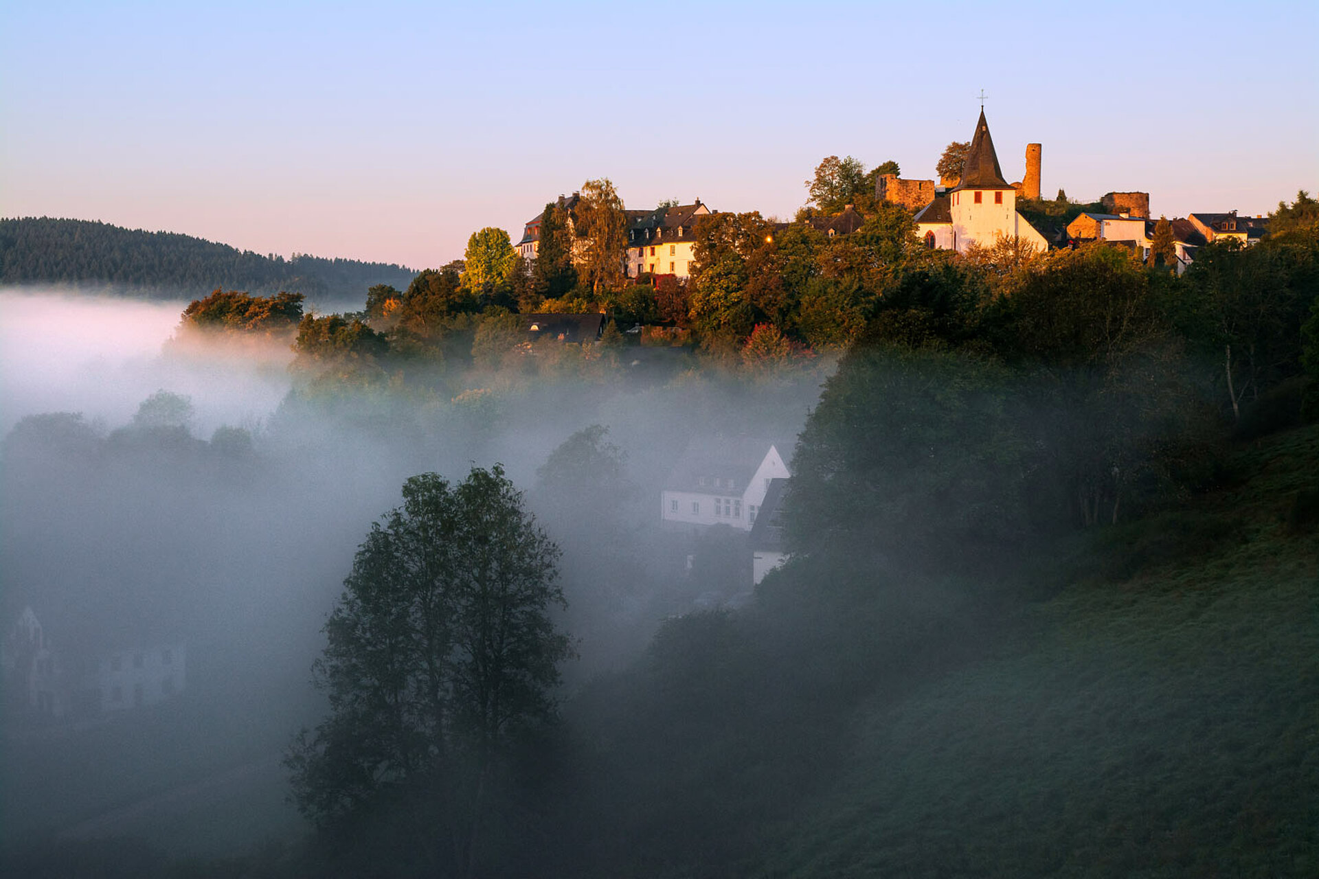 Der historische Ortskern von Dahlem-Kronenburg im Nebel bei Sonnenaufgang.