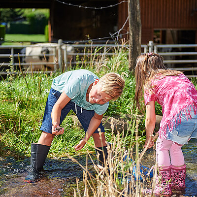 Junge und Mädchen spielen im Bach auf einem Bauernhof