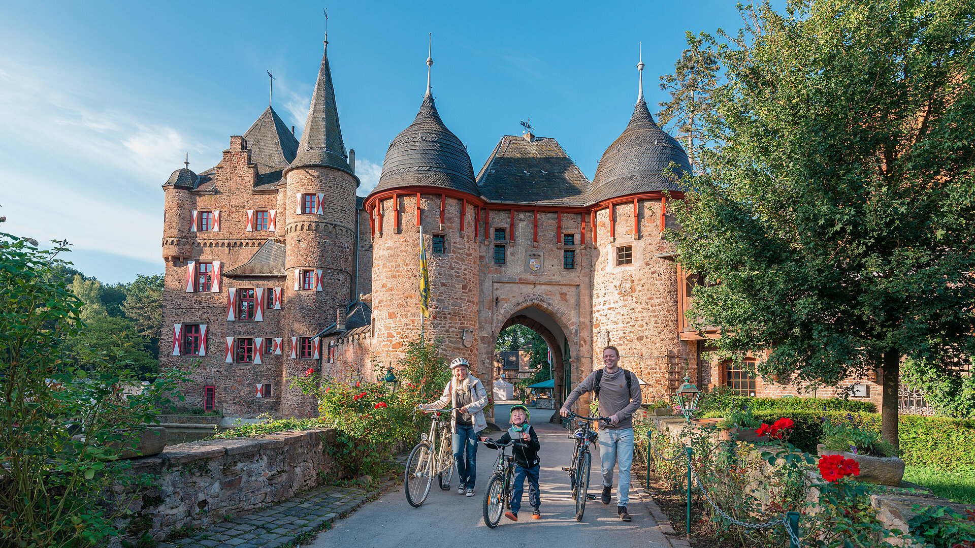 Eine junge Familie mit Rädern verlässt die Burg Satzvey durch das Tor