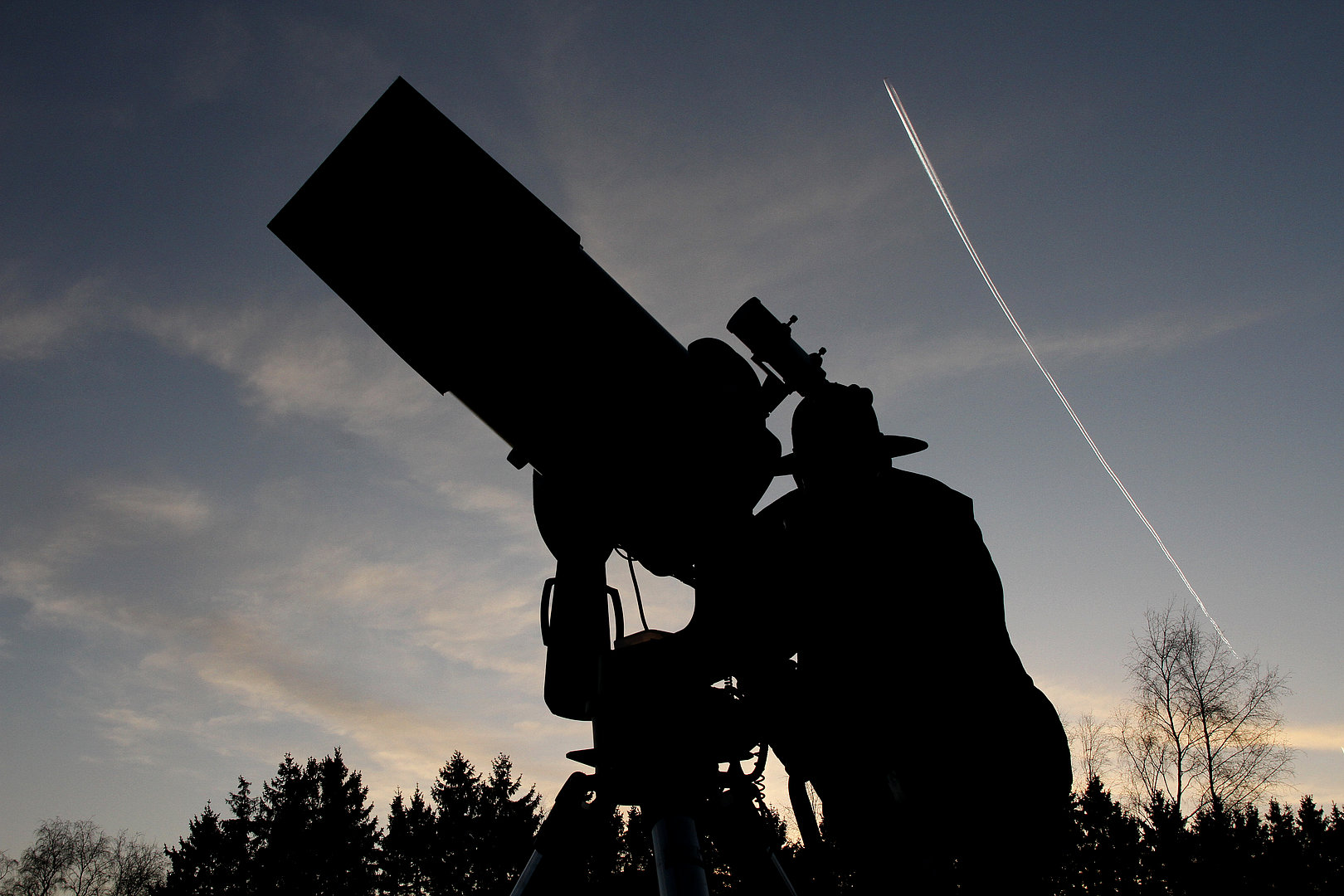 Nachtfoto von einem Mann mit Hut, der durch ein Teleskop schaut