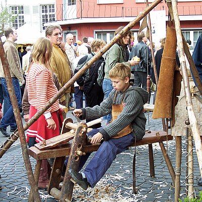 Auf einem mittelalterlichen Markt probieren zwei Kinder alte handwerksgeräte aus