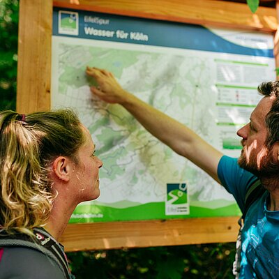 Wanderer stehen an einer Informationstafeln an den EifelSchleifen und EifelSpuren