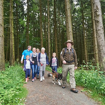 Eine Familie wandert gemeinsam mit einem Ranger durch einen Wald des Nationalpark Eifel