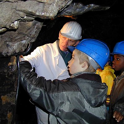 ein Bergmann erklärt Kindern etwas im Bergwerk